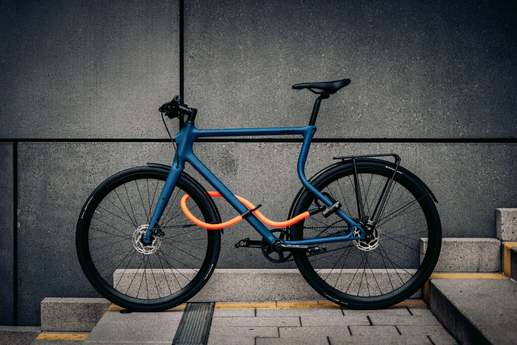Blue bike in front of gray wall securely locked with tex–lock eyelet in  orange