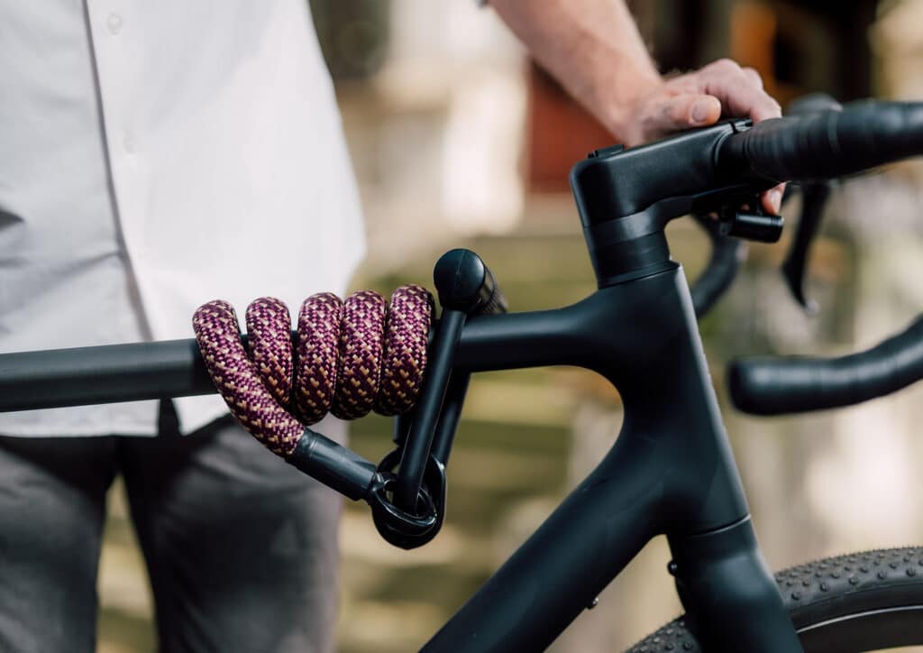 tex–lock eyelet in chateau red with X-lock flexibly wrapped around a bike's top tube, male model in background