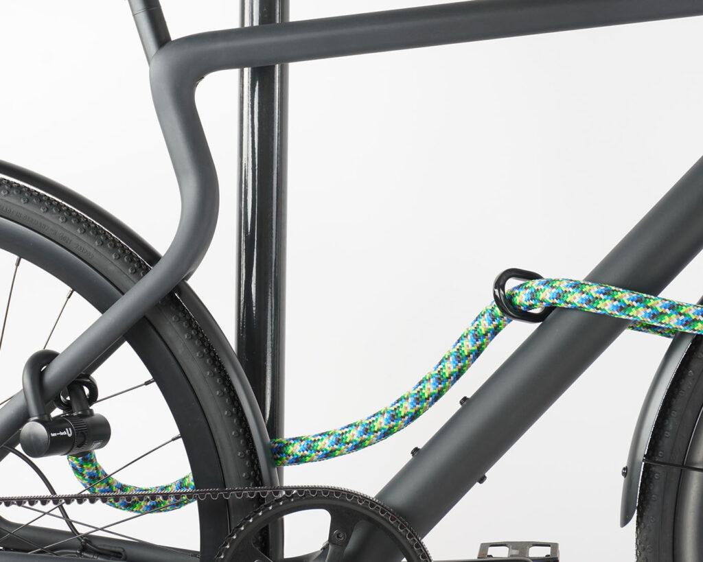 Small U-lock with extension made of colorful textile secures front and rear wheel at the same time on the bike stand